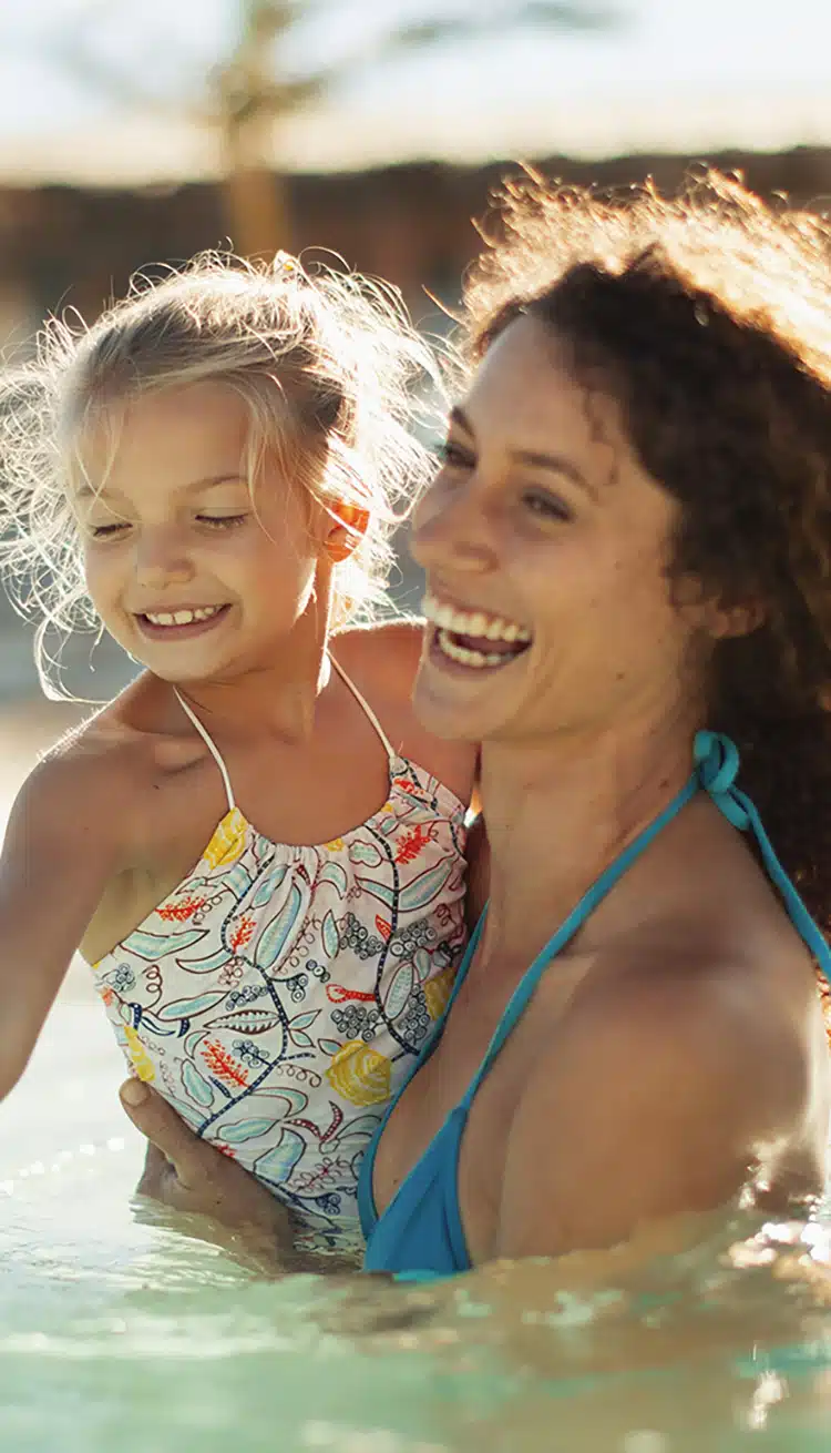 Happy mother and daughter swimming in sunny ocean